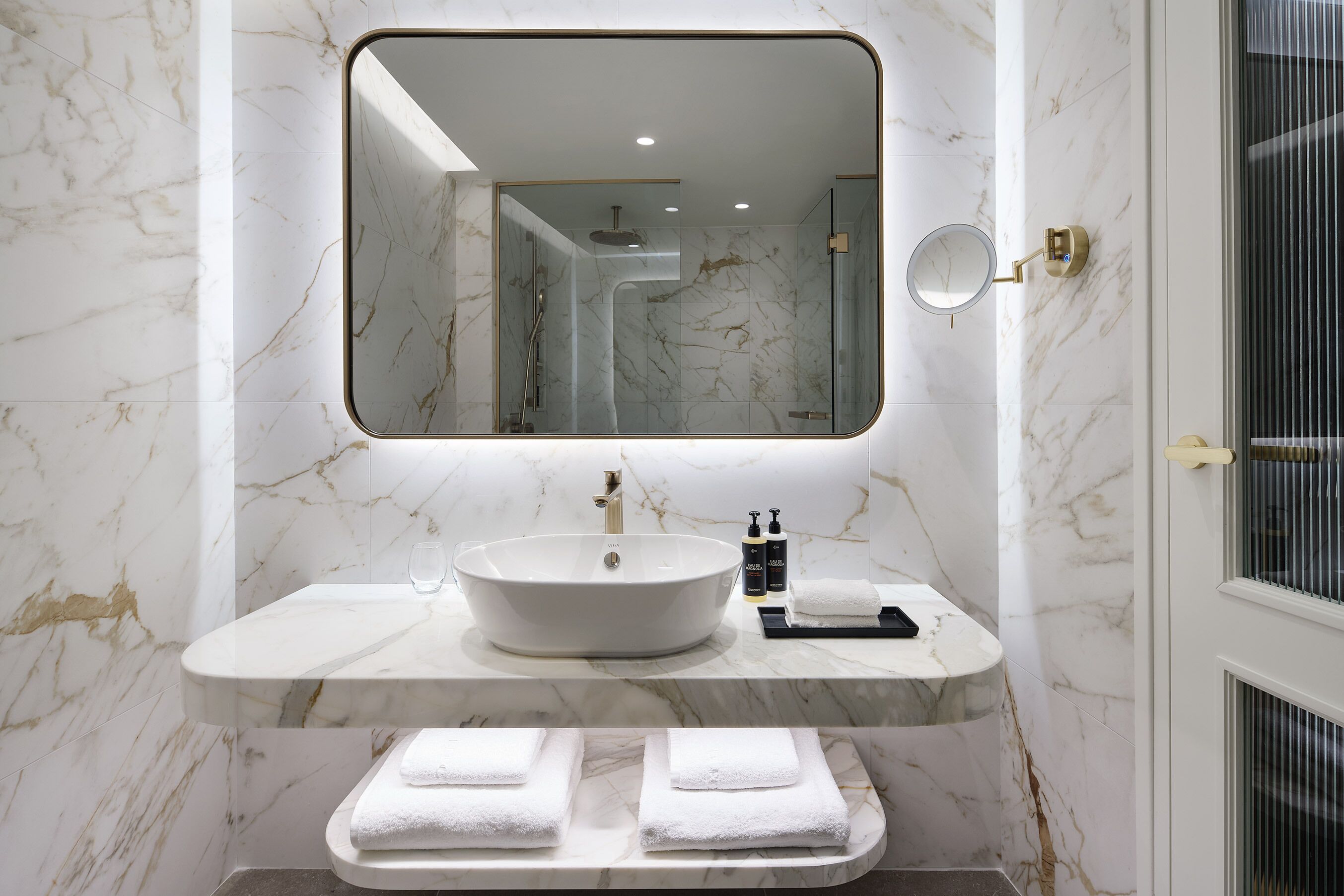 A bathroom with a marble vanity, a large mirror, a sink, and a towel rack.