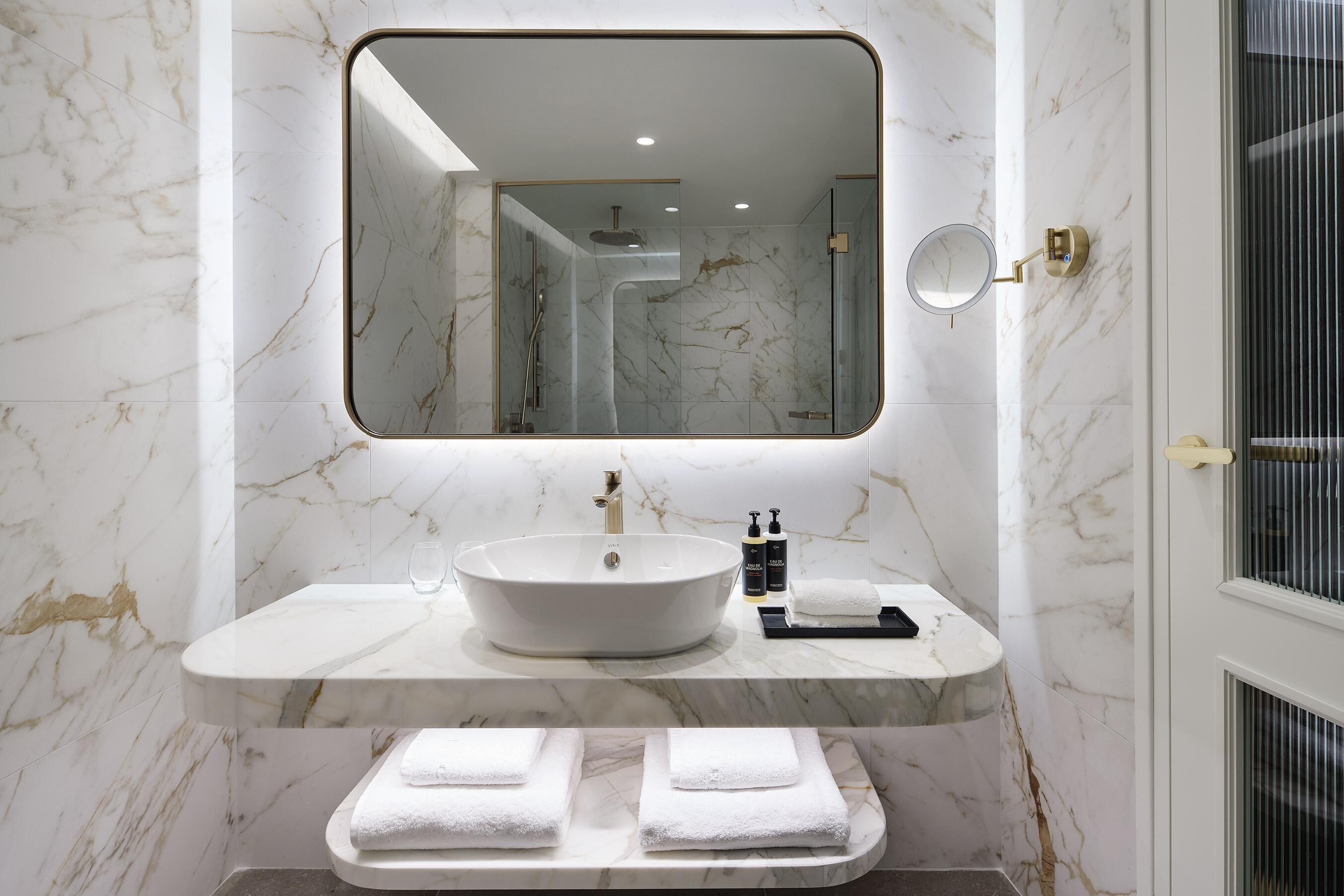 A bathroom with a marble vanity, a large mirror, a sink, and a shower area.