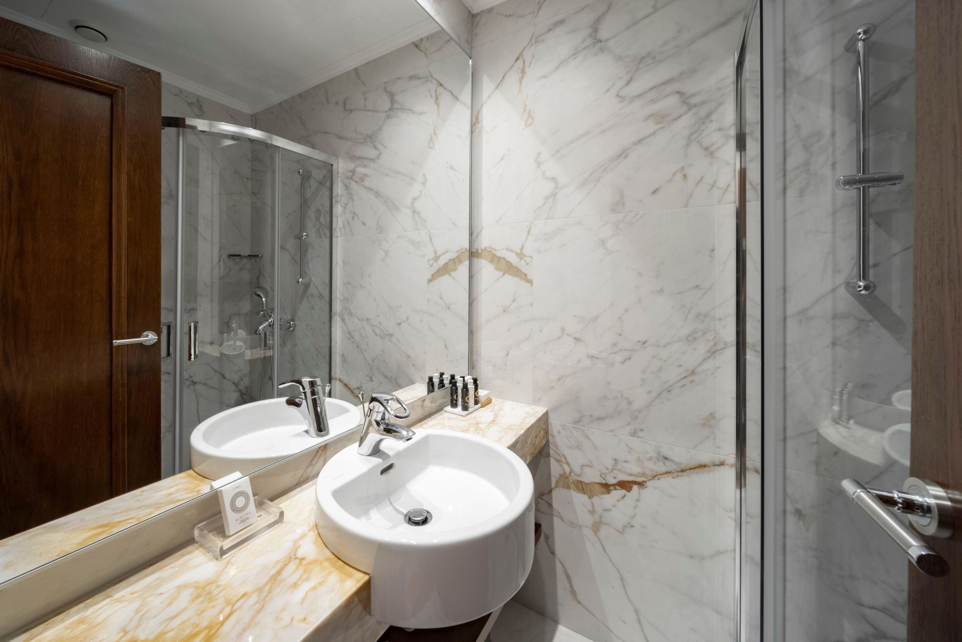 A modern bathroom with two sinks, a glass shower enclosure, and marble walls.
