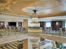 A grand lobby with a large chandelier, a checkered floor, and a balcony with a railing.