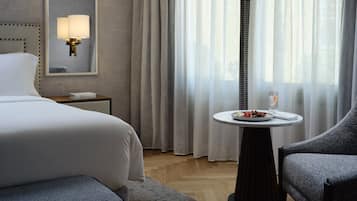 Ein Hotelzimmer mit einem Bett, einem Nachttisch mit Lampe, einem kleinen runden Tisch mit Obstteller und einem Sessel.