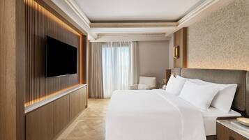 A hotel room with a large bed, a flat-screen TV mounted on the wall, a wooden panel design, and a large window with curtains.