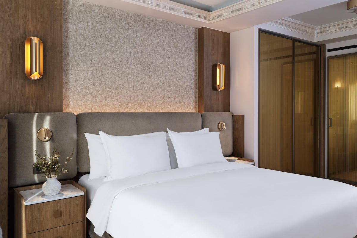 A neatly made bed with white linens, a wooden headboard, and a nightstand with a vase of flowers.