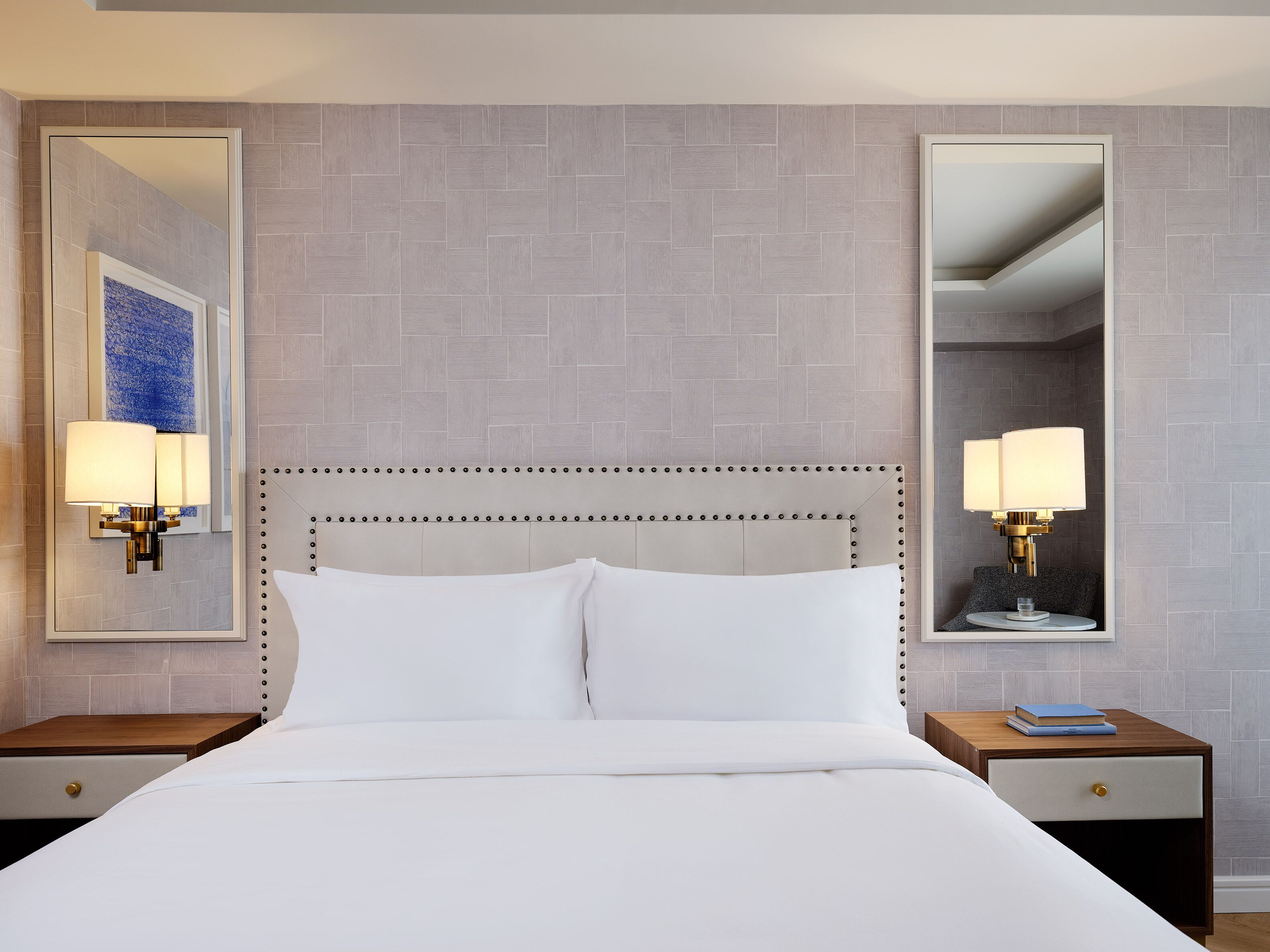 A hotel room with a large bed, two bedside tables, a mirror, and a wall-mounted light fixture.