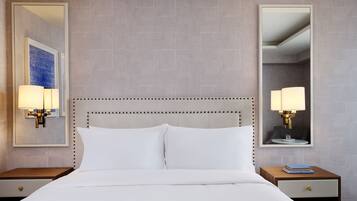A hotel room with a large bed, two bedside tables, a mirror, and a wall-mounted light fixture.