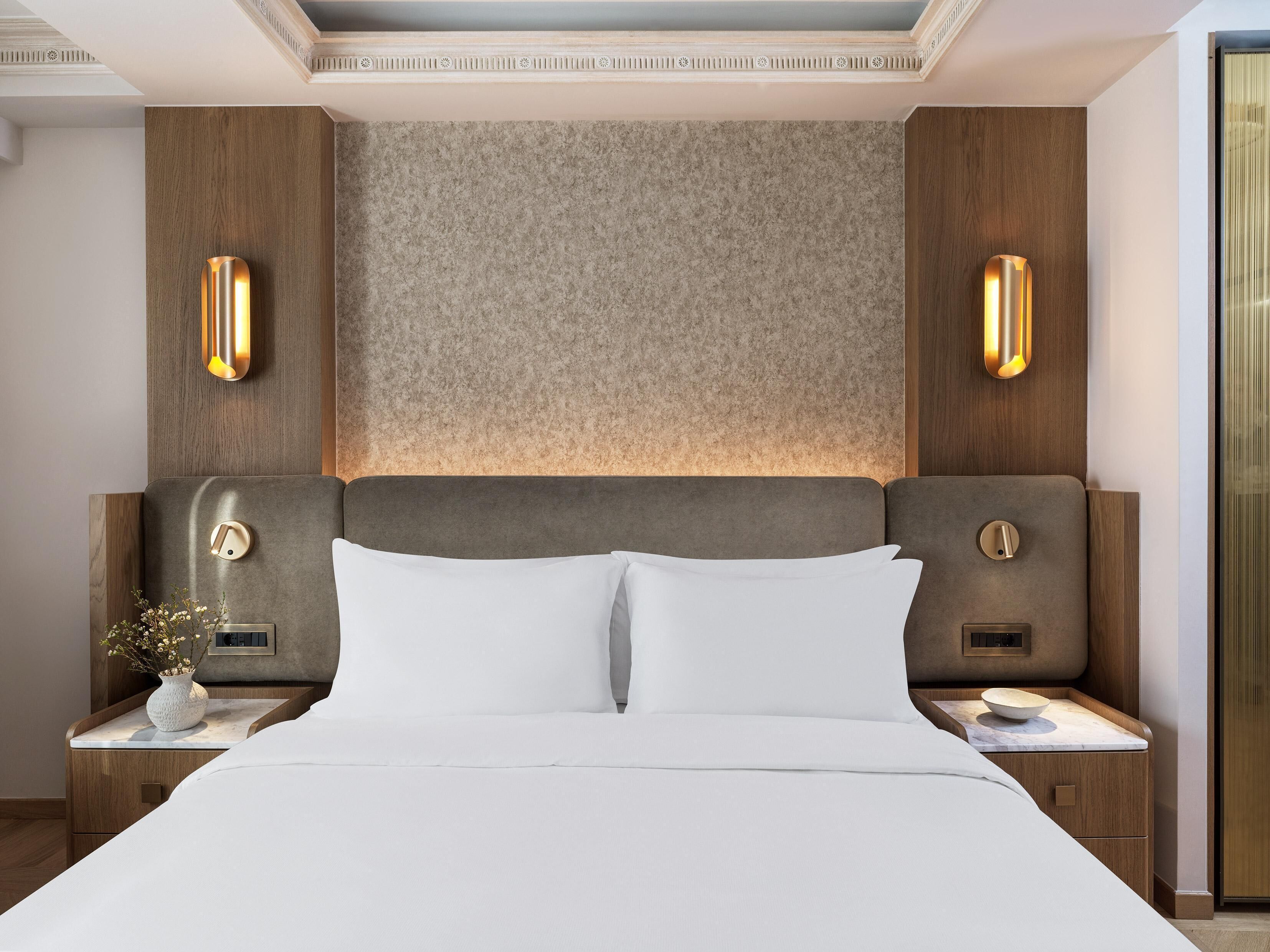 A modern hotel room with a large bed, wooden headboard, and two bedside tables with lamps.