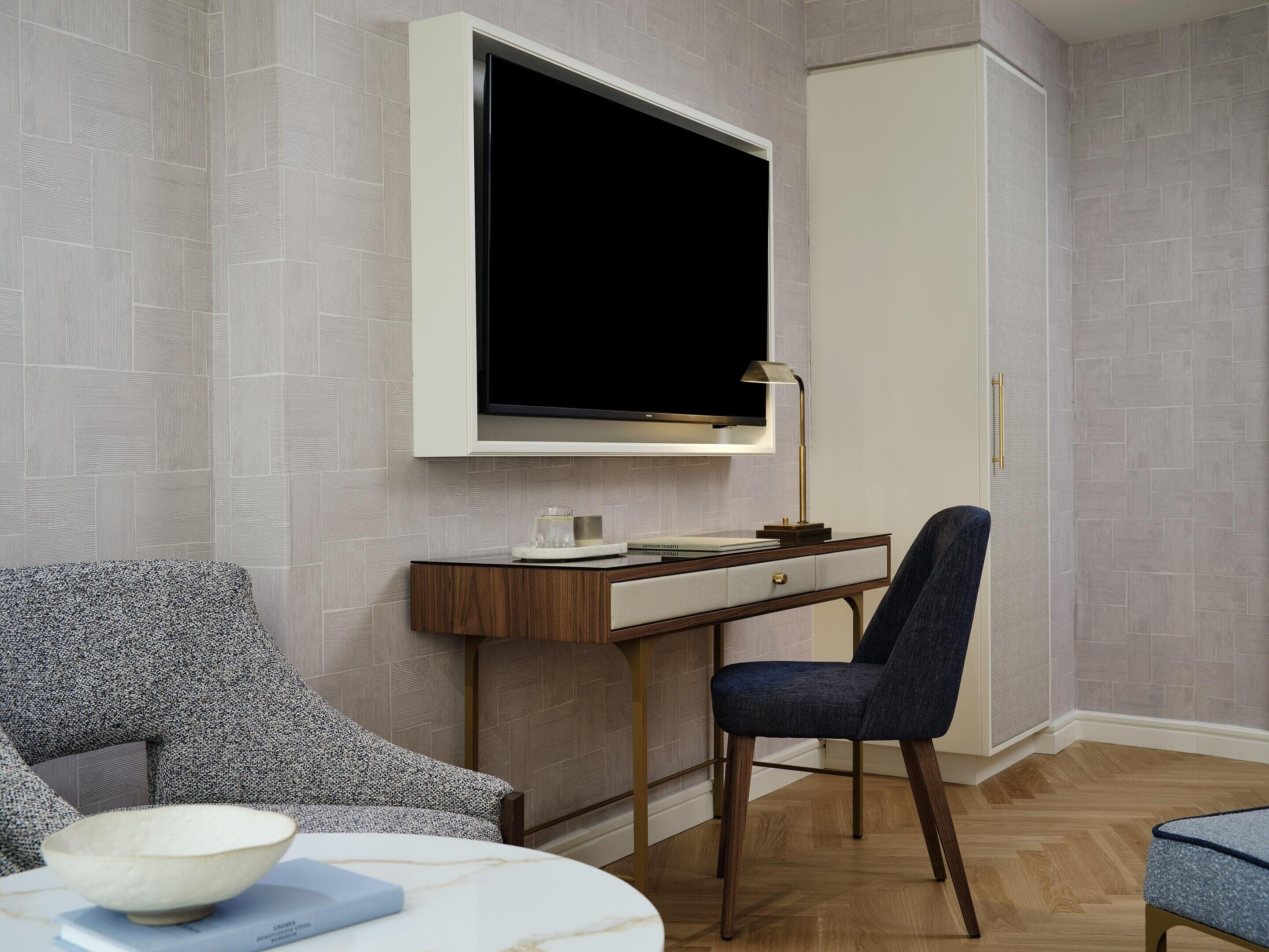 Una habitación moderna con un televisor de pantalla plana en la pared, un escritorio con lámpara, una silla y una mesita con un bol.