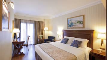 A hotel room with a large bed, a desk with a chair, a nightstand, and a painting on the wall.