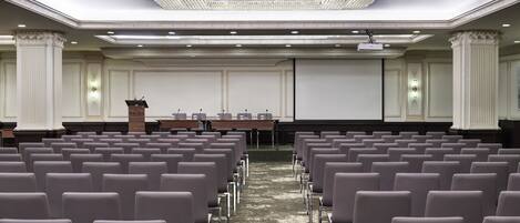 A conference room with rows of chairs, a podium, and a projector screen.