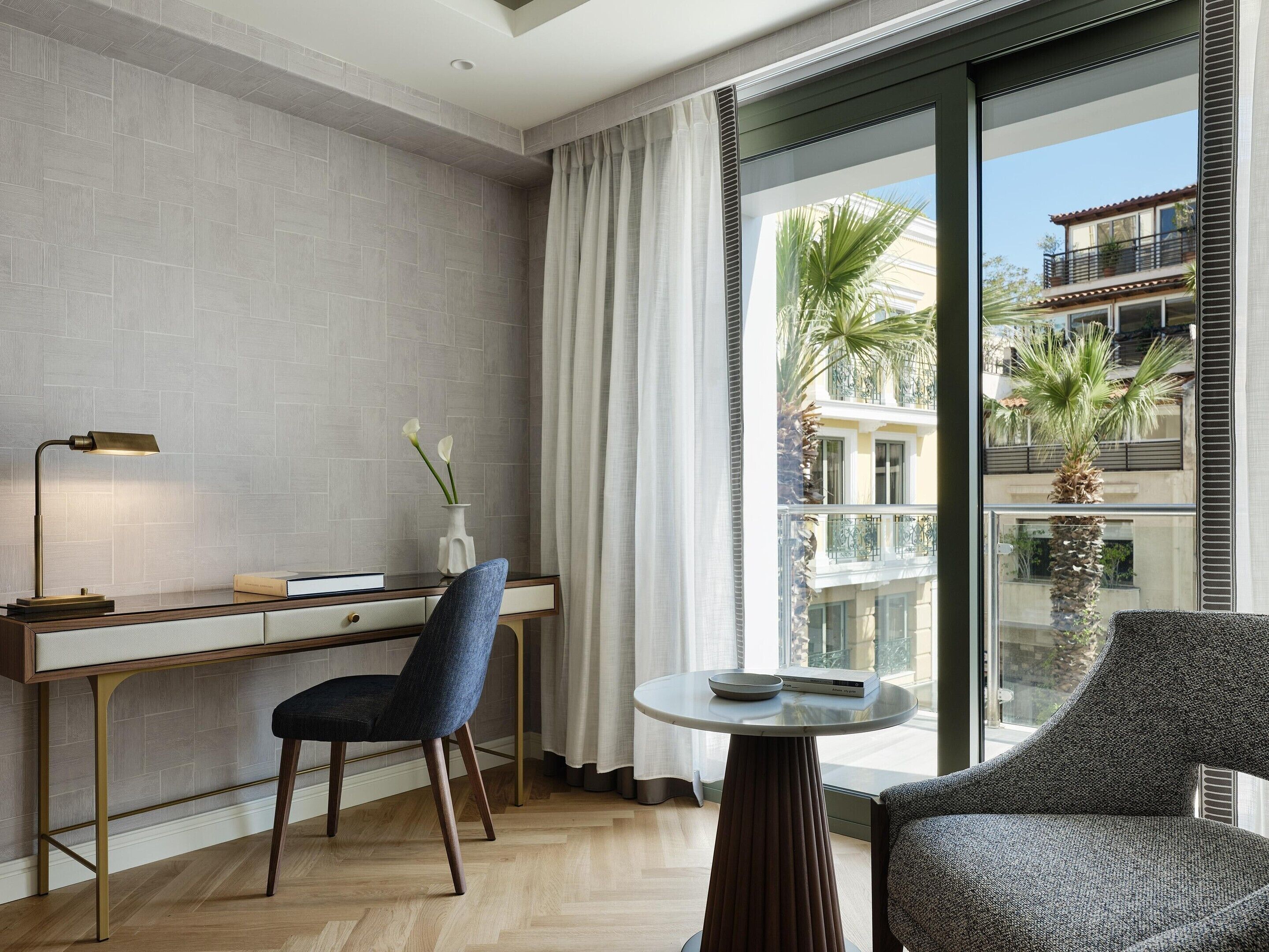 A modern hotel room with a desk, chair, and a round table with a book and a bowl.