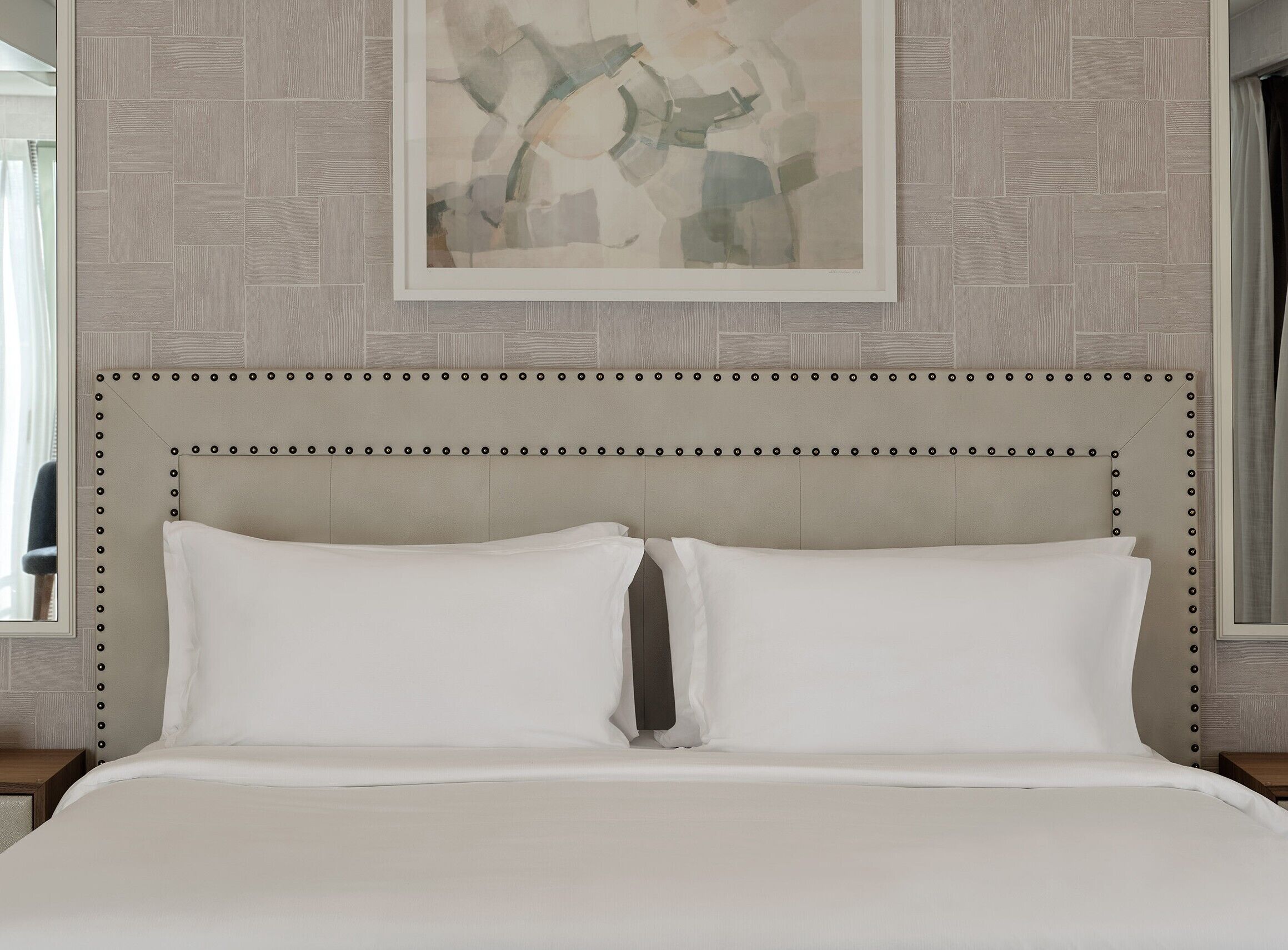 A bed with a headboard, a framed abstract painting above it, and a patterned wall.