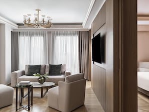 A modern hotel room with a large TV, a sofa set, a small table with a vase, and a wooden panel wall.
