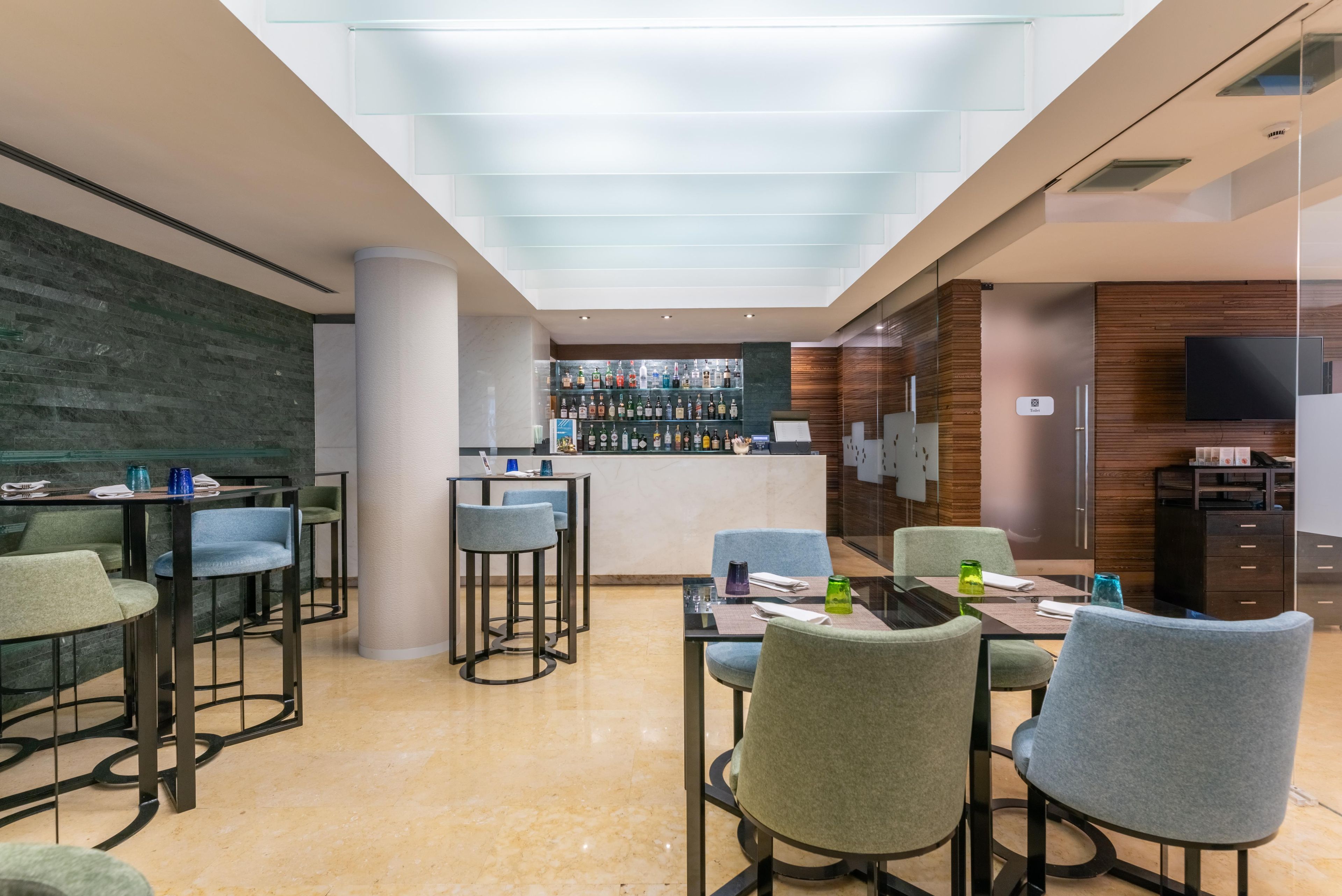 A modern hotel lobby with a bar area, seating arrangements, and a visible restroom sign.