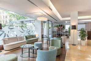 A modern lobby with a sofa, armchairs, a coffee table, and a bookshelf. - Hilton Garden Inn Rome Claridge (Rome)
