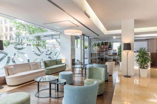 A modern lobby with a sofa, armchairs, a coffee table, and a bookshelf.