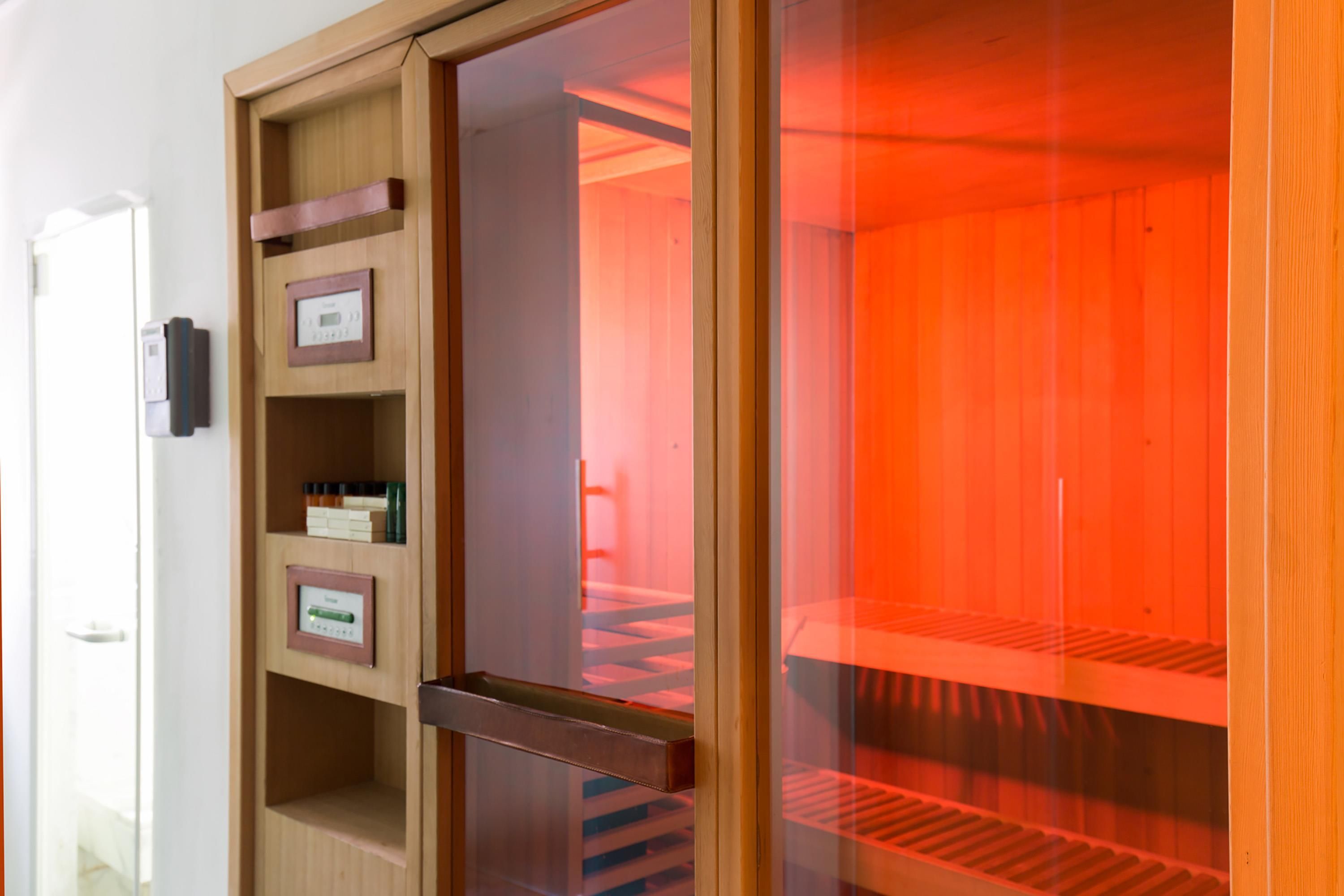 A sauna room with a wooden door, a control panel, and a glass partition.