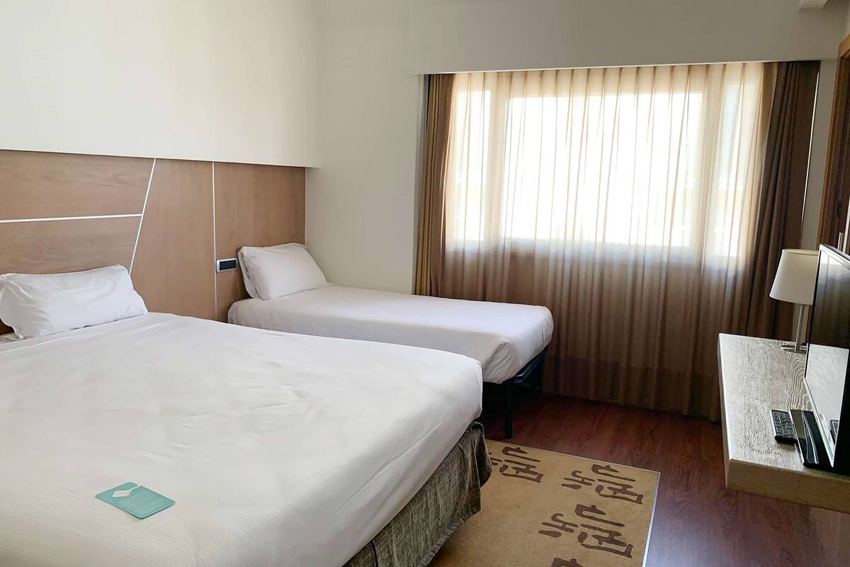 A hotel room with two beds, a desk with a lamp, and a window with curtains.