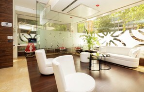 A modern office space with white furniture, a glass partition, and a view of greenery outside.