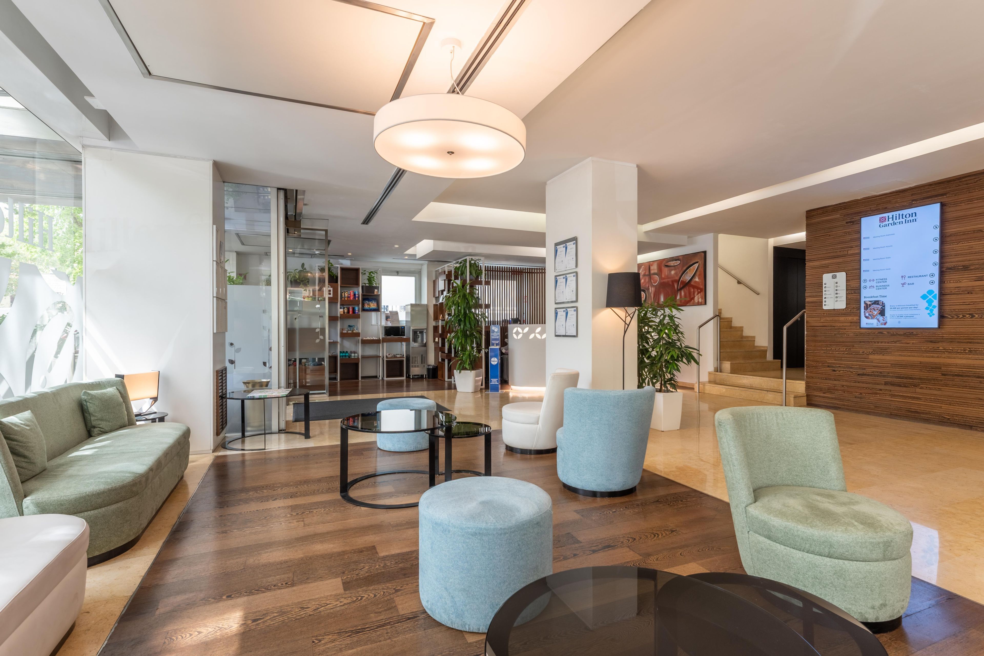 Un moderno vestíbulo de hotel con una recepción, una zona de estar y una escalera que lleva a otras plantas.