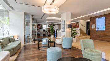 Un moderno vestíbulo de hotel con una recepción, una zona de estar y una escalera que lleva a otras plantas.