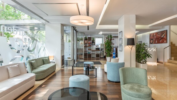 A modern hotel lobby with a seating area, a glass wall with a view, and a staircase.