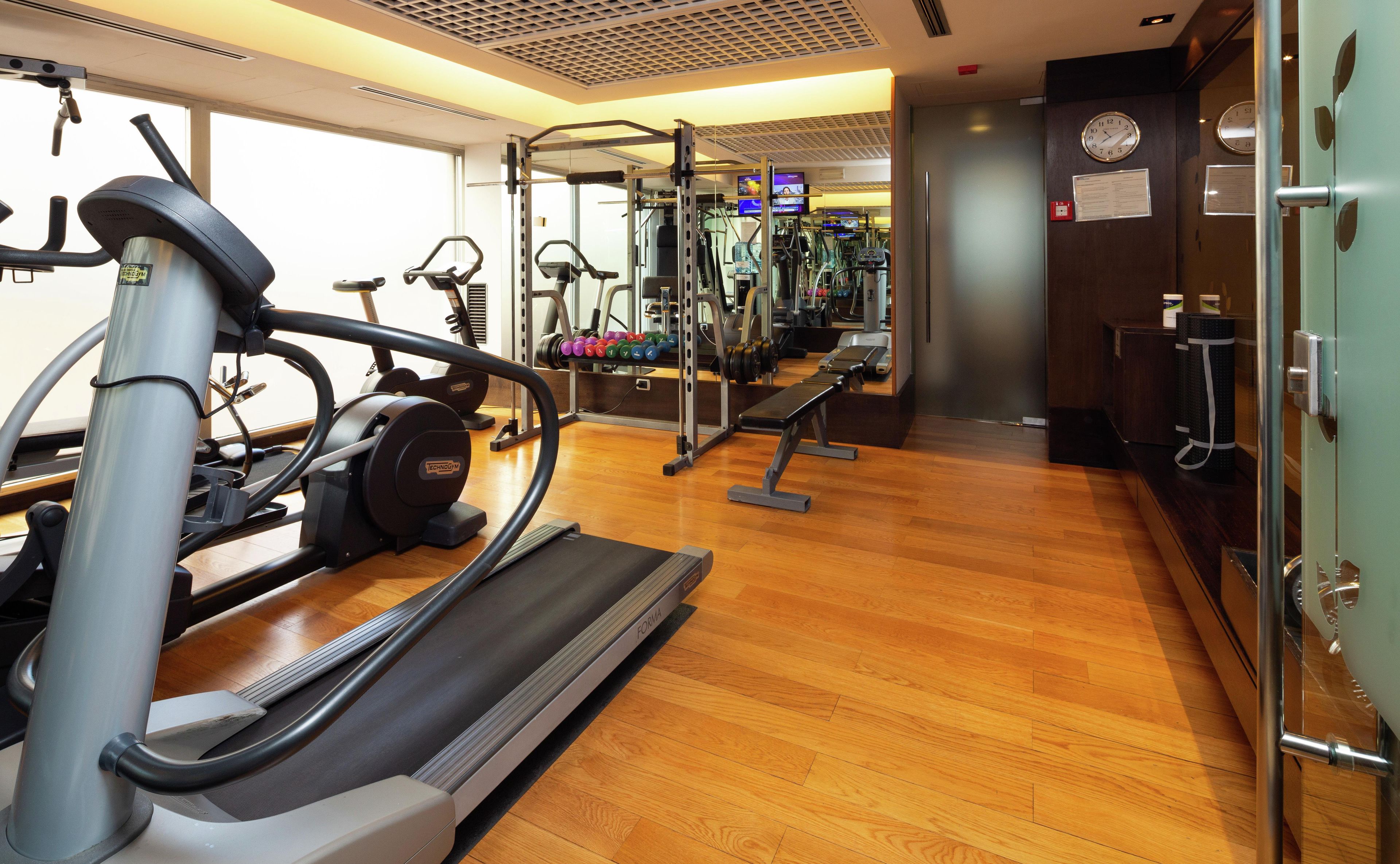 A gym with cardio equipment, weight machines, and a wooden floor.