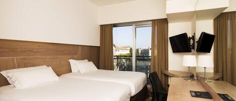 A hotel room with two beds, a desk with a computer, a TV, and a view of the city.