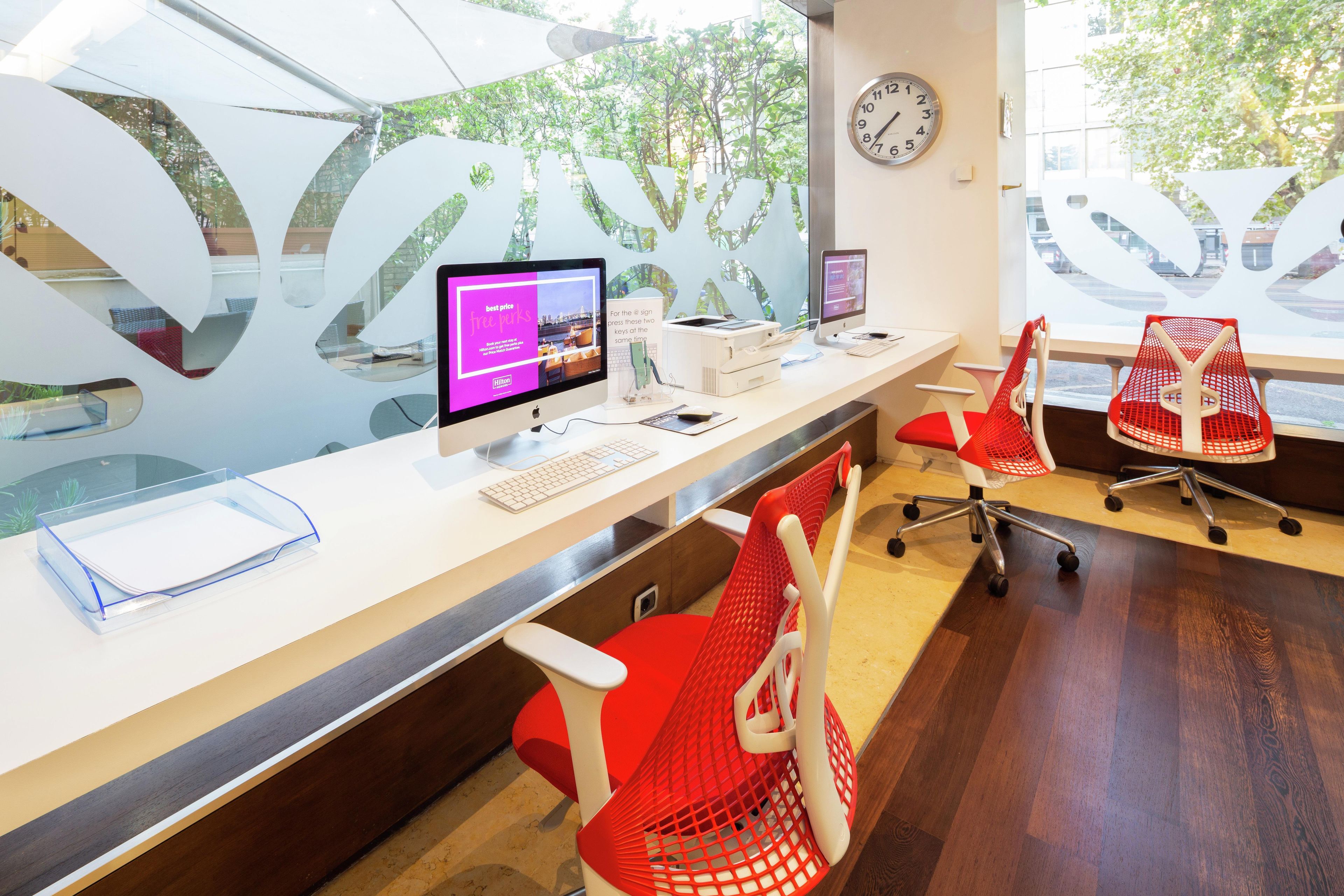 Un espace de bureau moderne comprenant un bureau, un ordinateur, une imprimante et des chaises à dossier en tissu rouge.