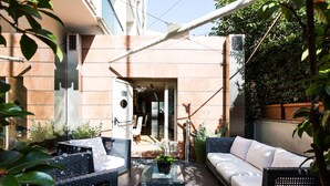 An outdoor patio area with wicker furniture, a glass table, and potted plants.