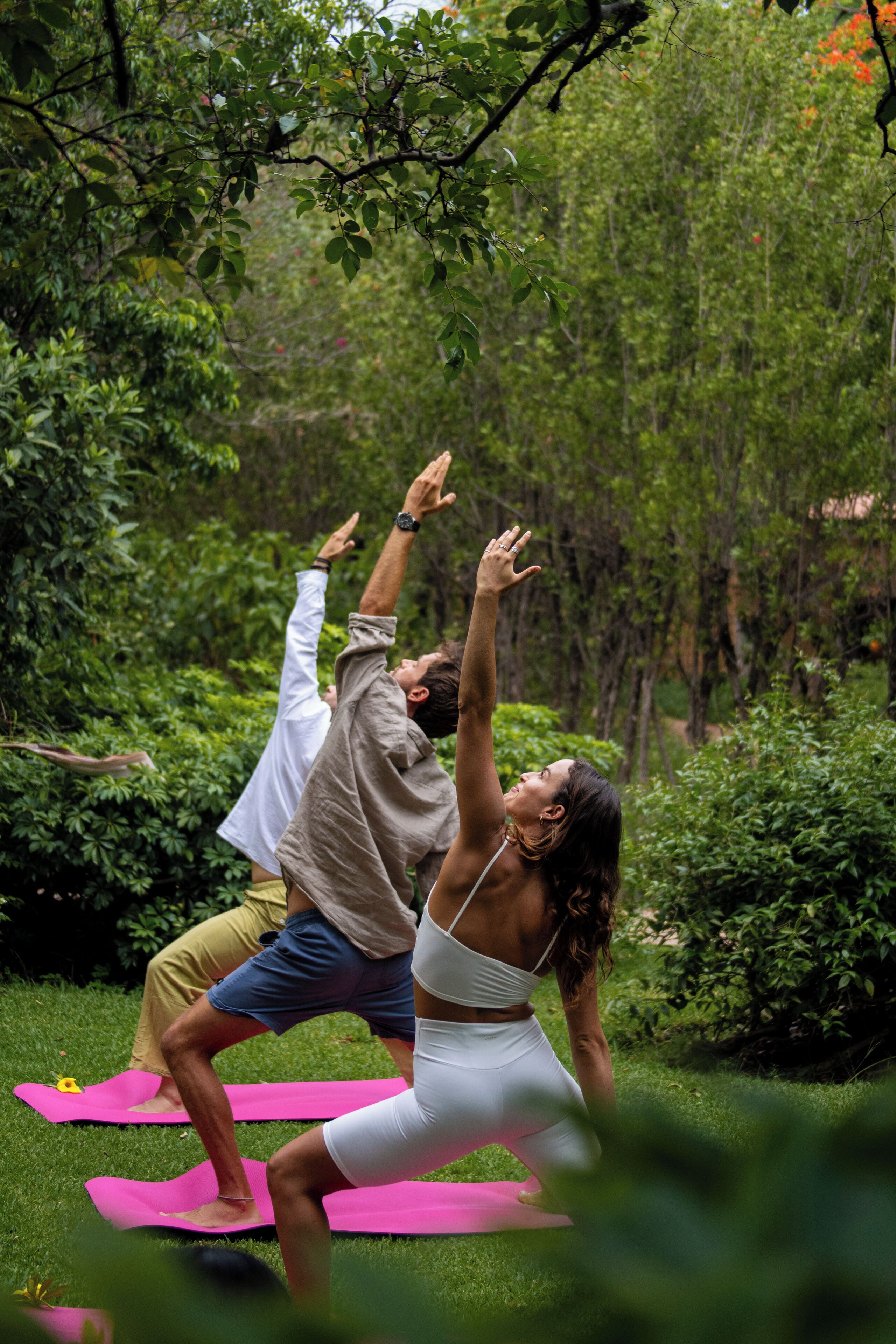 Two people practicing yoga on a grassy area surrounded by dense greenery.