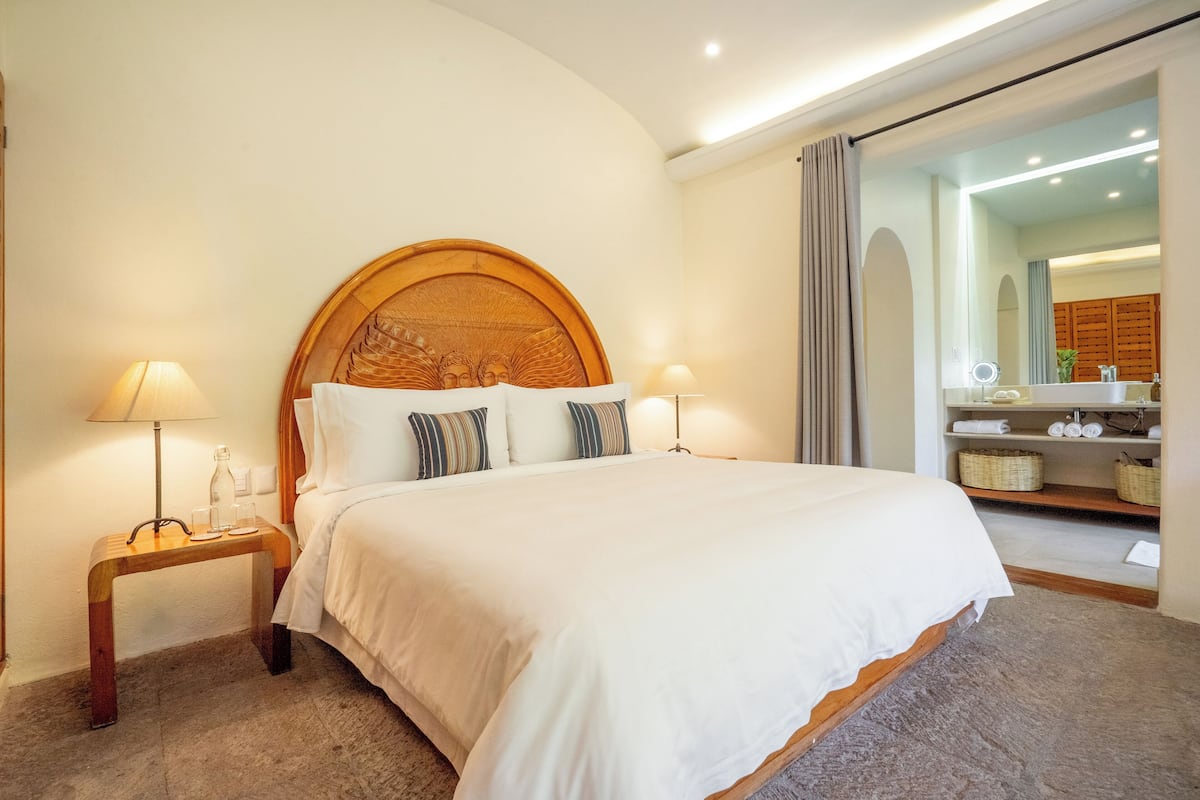 A neatly made bed with a wooden headboard, two bedside lamps, and a small wooden nightstand with a lamp and a bottle.
