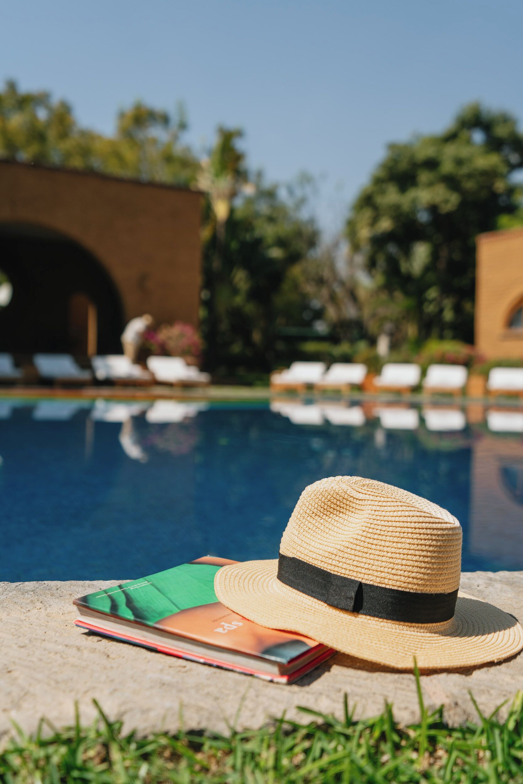 A poolside setting with a straw hat and a book on a stone surface.
