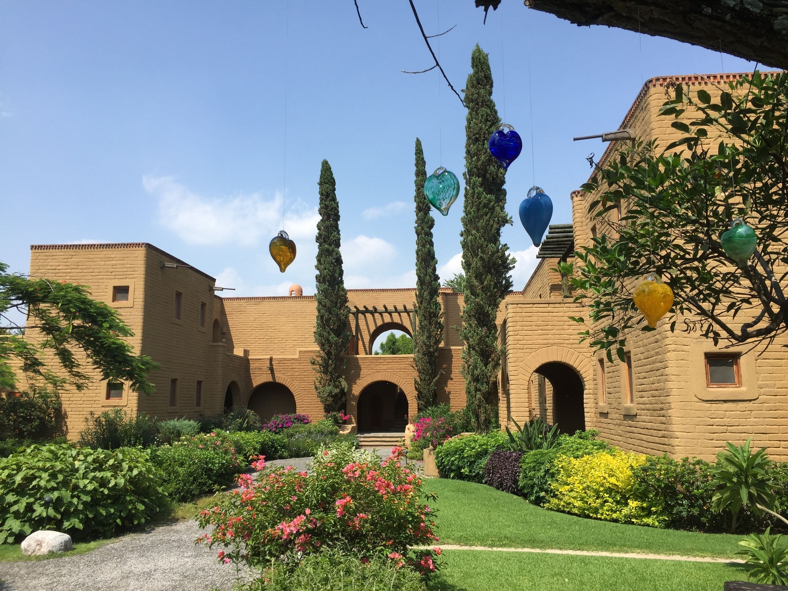 A courtyard with a brick building, arches, and a variety of plants and flowers.