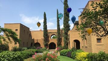 A courtyard with a brick building, arches, and a variety of plants and flowers.
