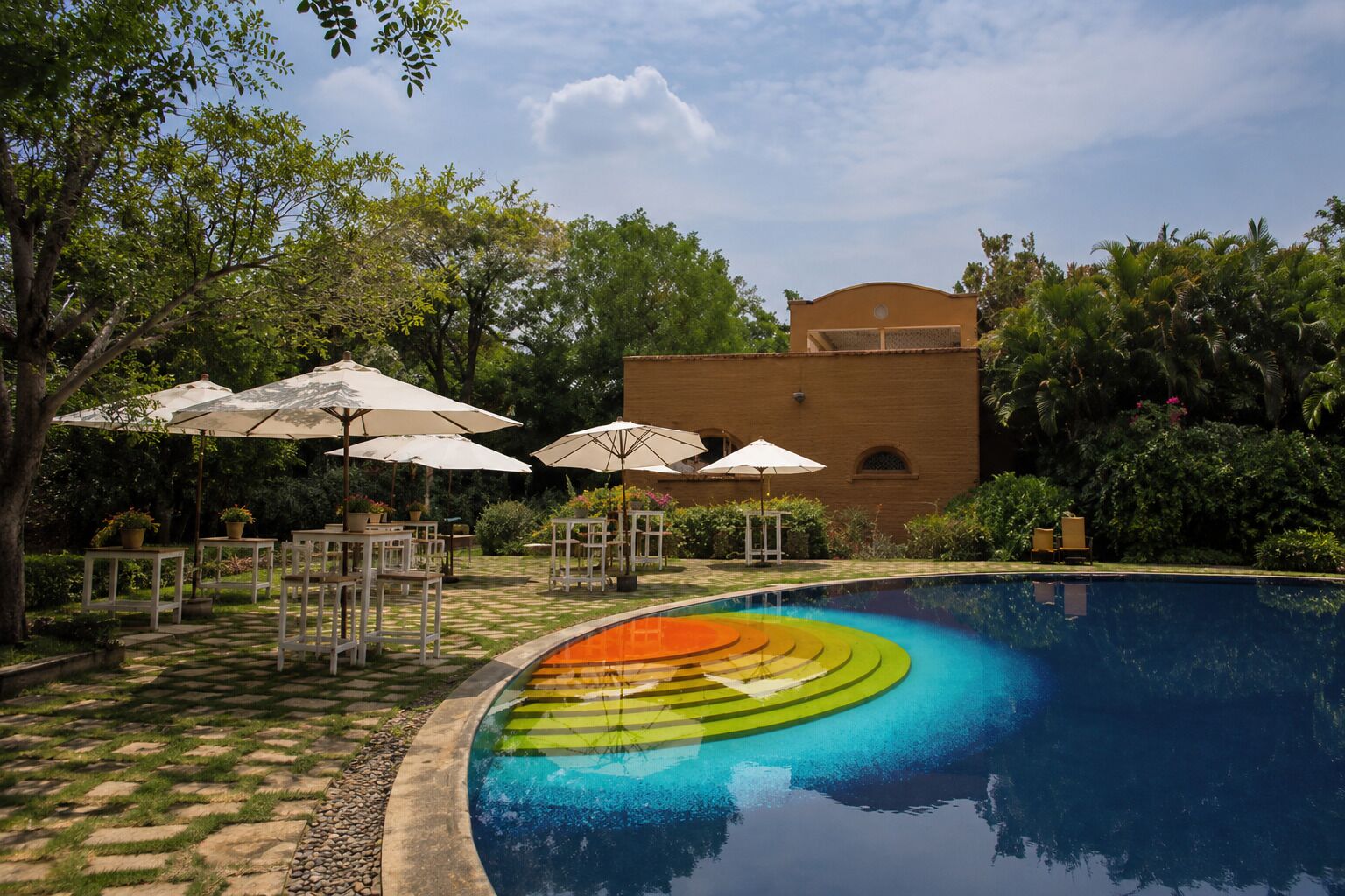 Una piscina con borde colorido, rodeada de mobiliario exterior y un edificio de ladrillo.