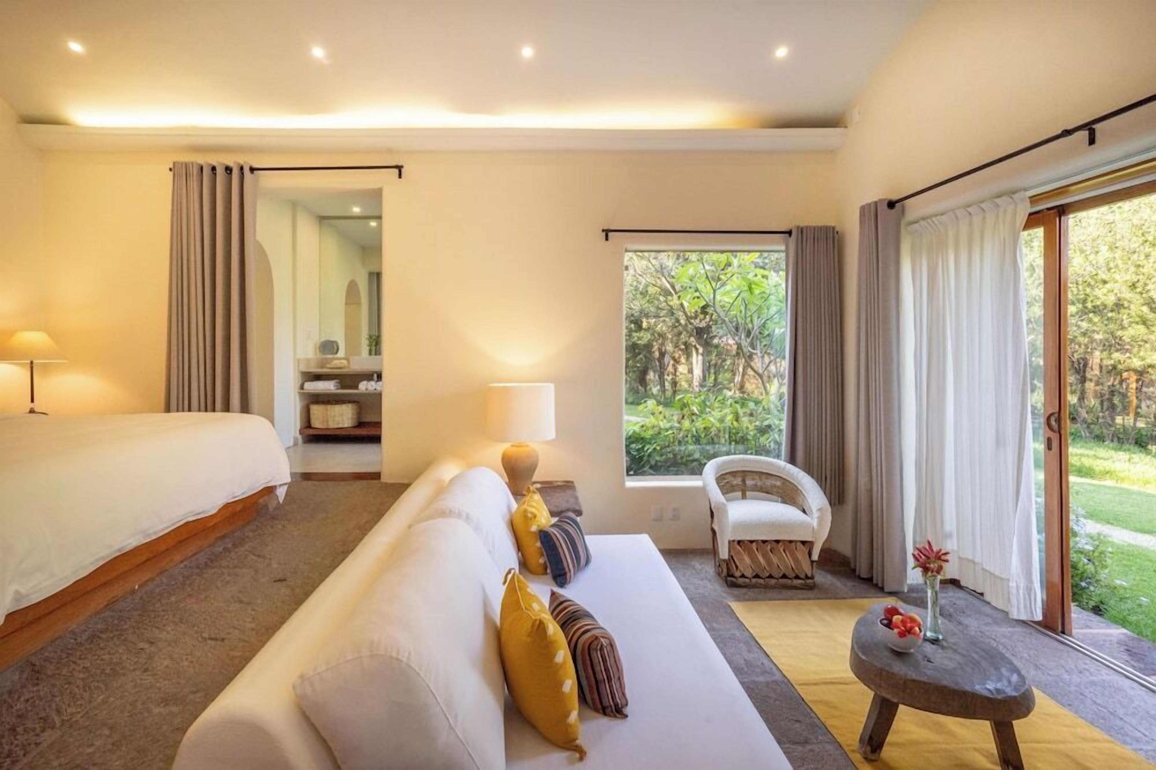 A hotel room with a bed, a sofa, a chair, a small table, and a window with curtains.