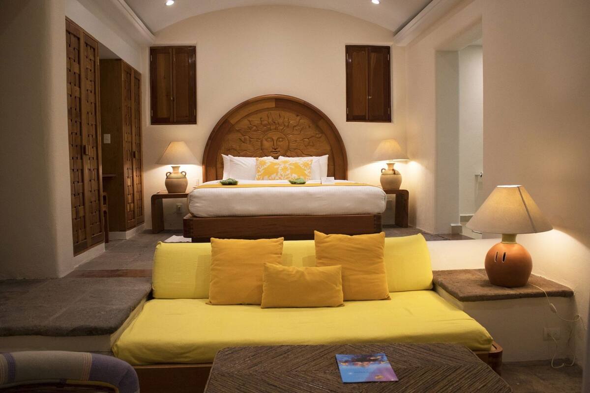 A bedroom with a large bed, two bedside tables with lamps, a sofa, and a wooden headboard.