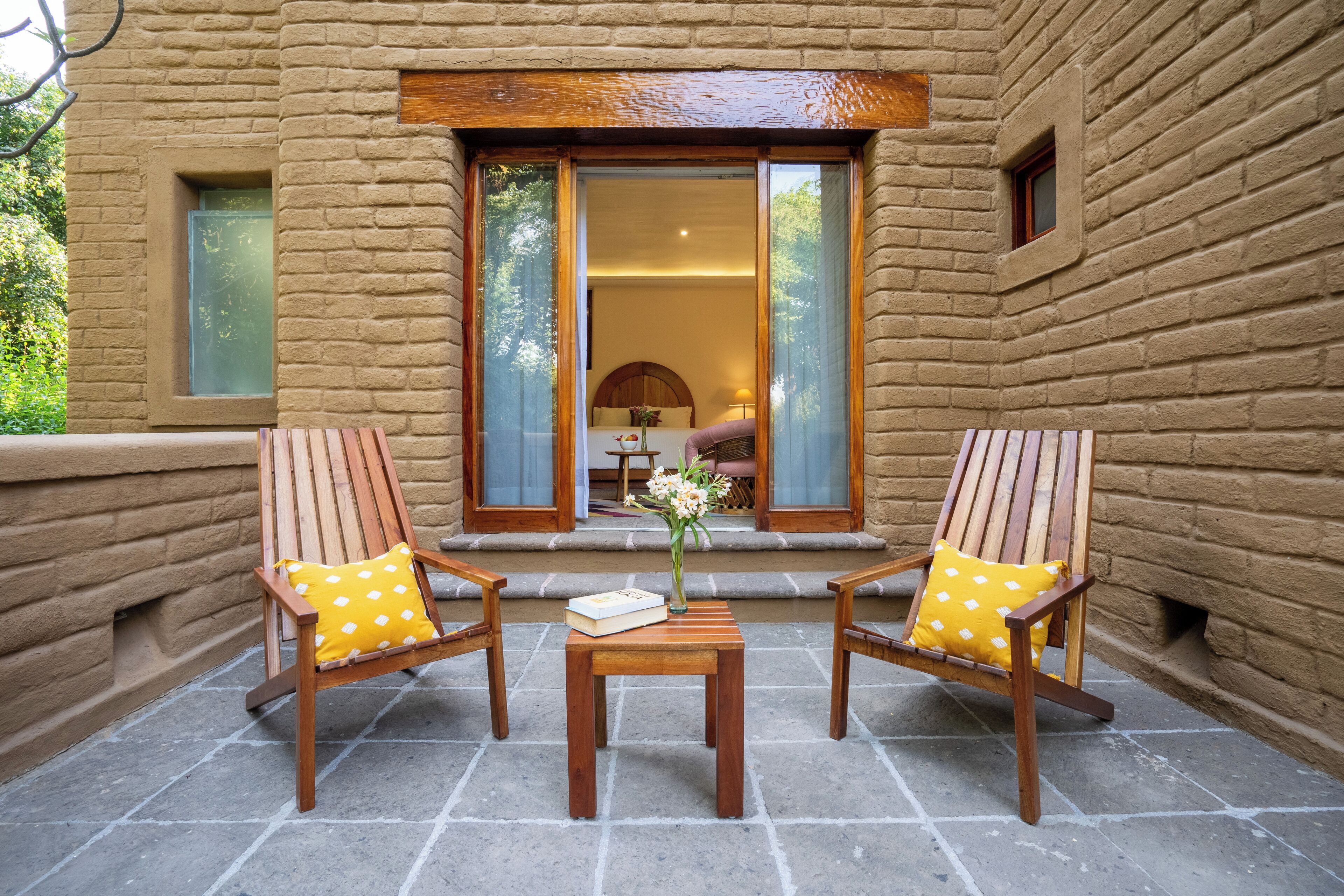 A wooden chair and table set on a stone patio with a brick wall and a glass door leading to an interior space.