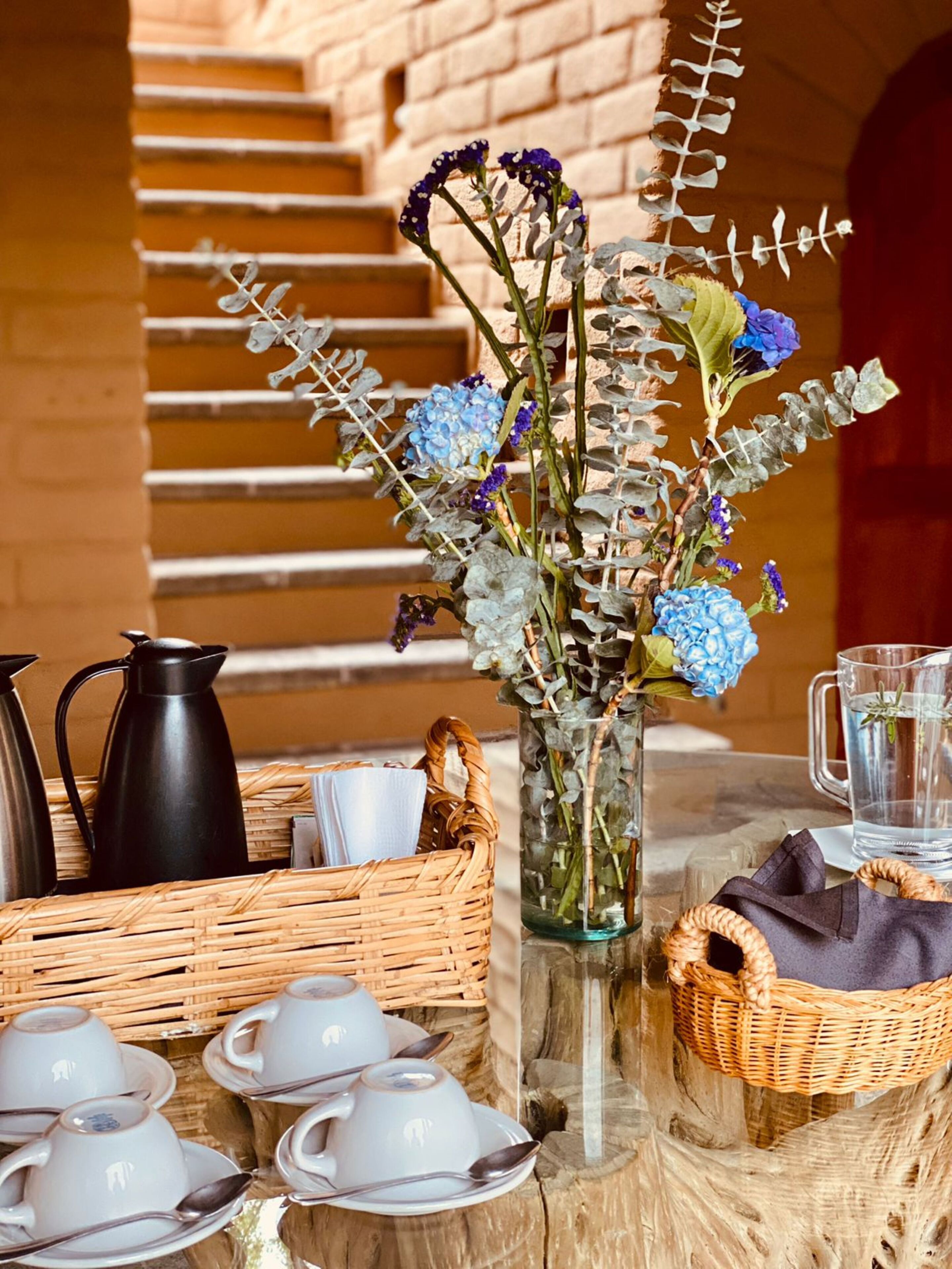 A table with a vase of flowers, tea set, and a coffee pot.