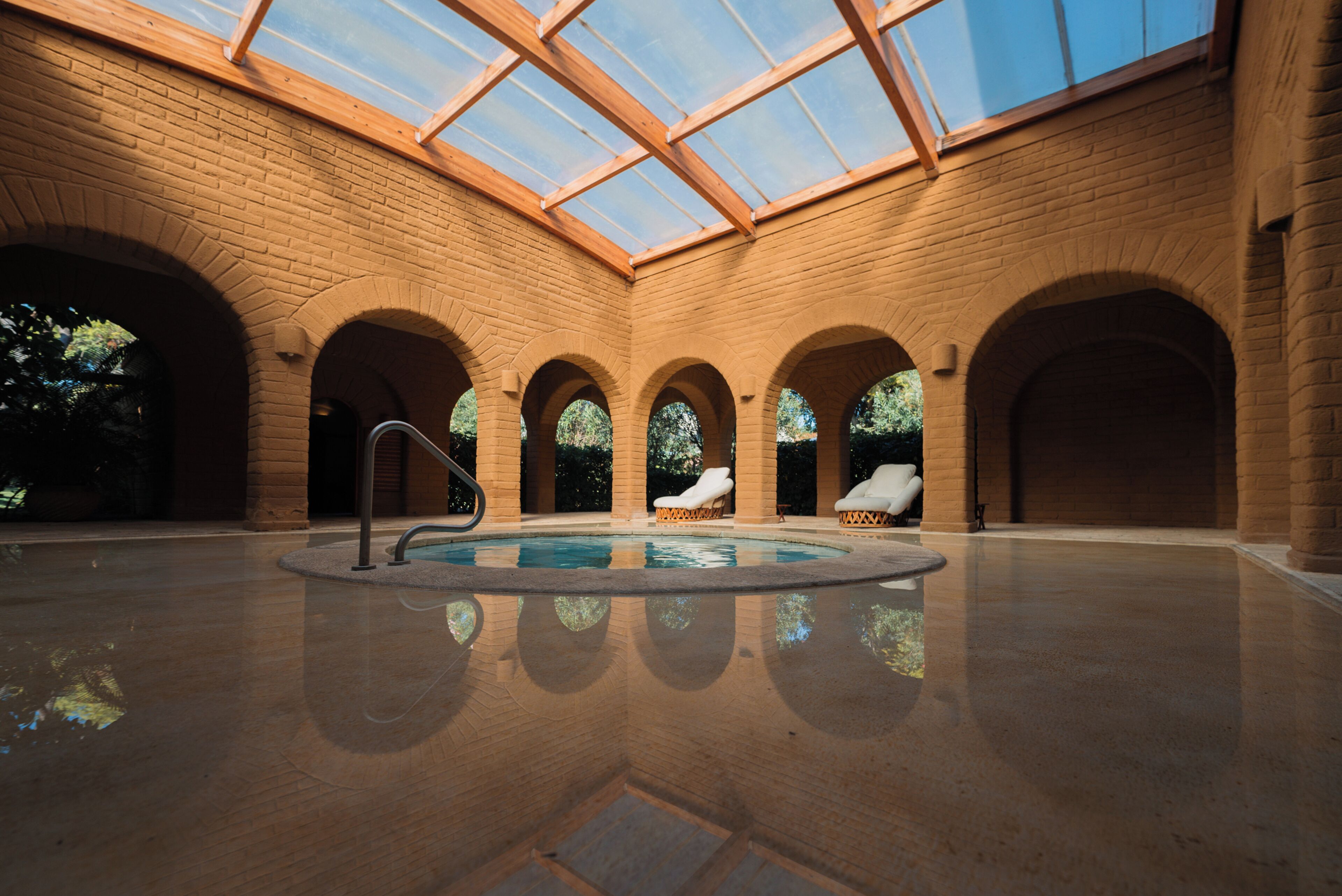 Una piscina interior con techo de vidrio, paredes de ladrillo y sillones de descanso.