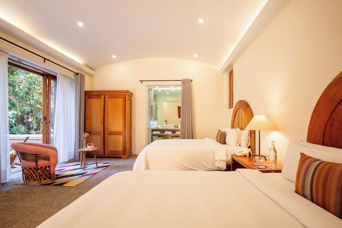 A hotel room with two beds, a wooden wardrobe, a small table with a lamp, and a chair.