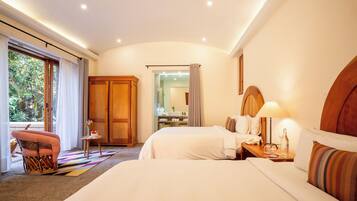 Una habitación de hotel con dos camas, un armario de madera, una mesita con lámpara y una silla.