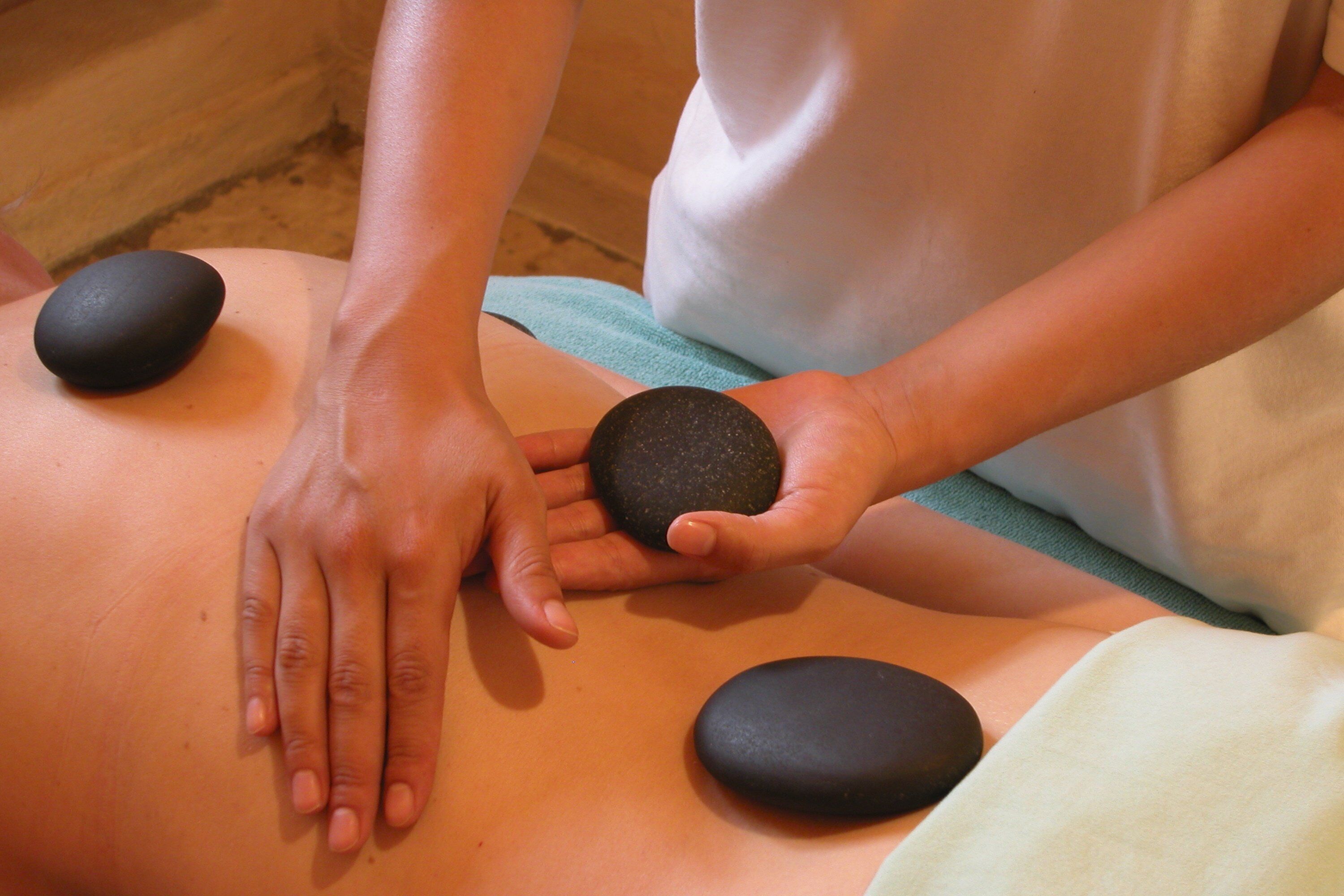 Een massagetherapie sessie waarbij een persoon een rugmassage ontvangt met zwarte stenen.