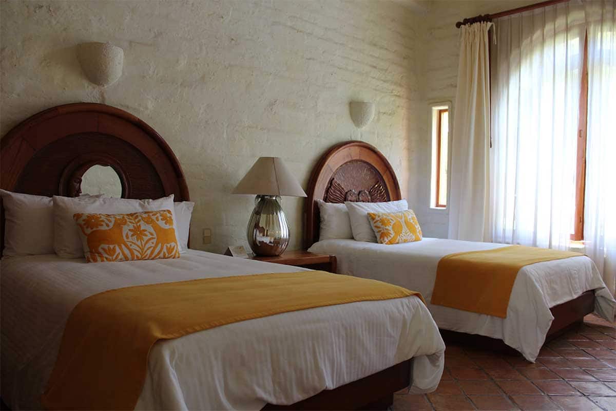 Two double beds with wooden headboards, a bedside table with a lamp, and a window with curtains.