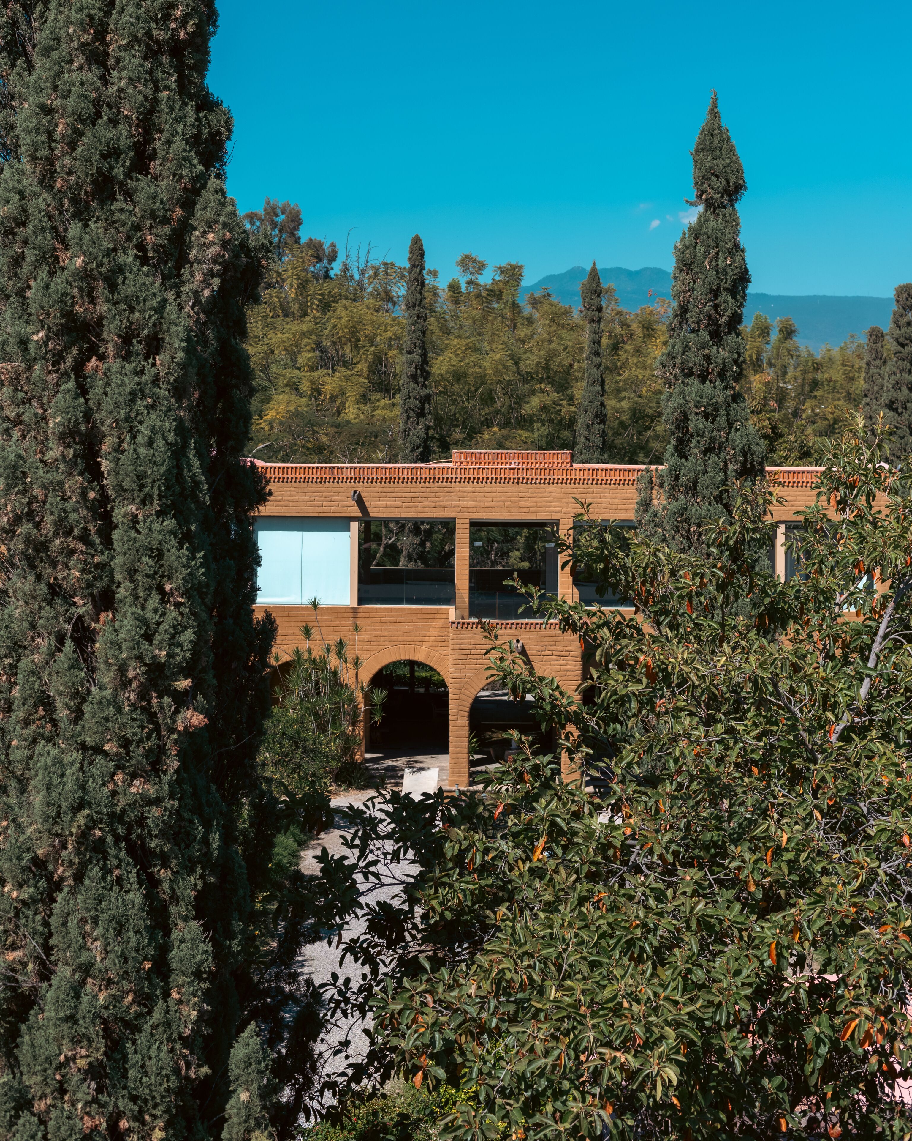 A building with a brick facade, arched entryways, and surrounded by dense trees.
