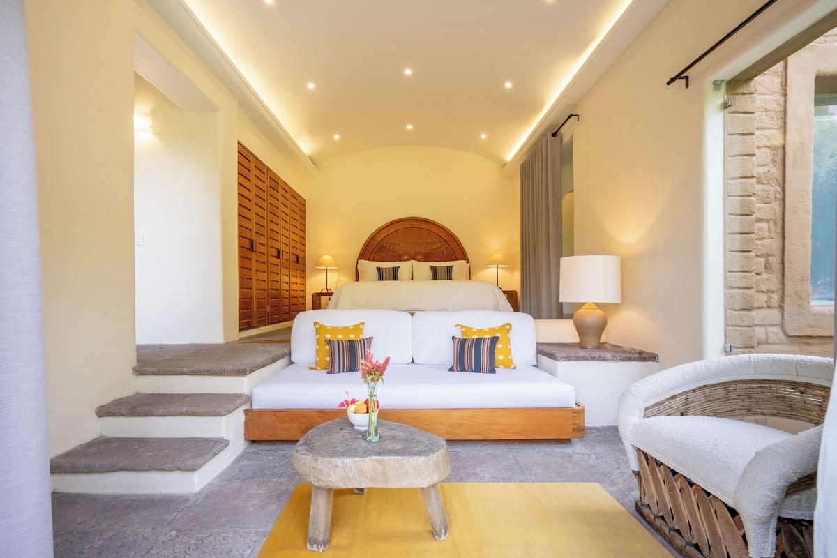 A cozy bedroom with a bed, a sofa, a small round table, and a wicker chair.