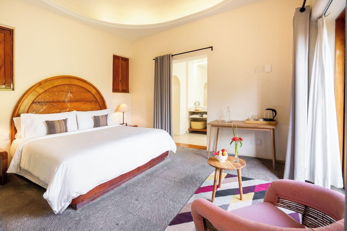 A hotel room with a large bed, a desk, a chair, and a small table with a vase of flowers.