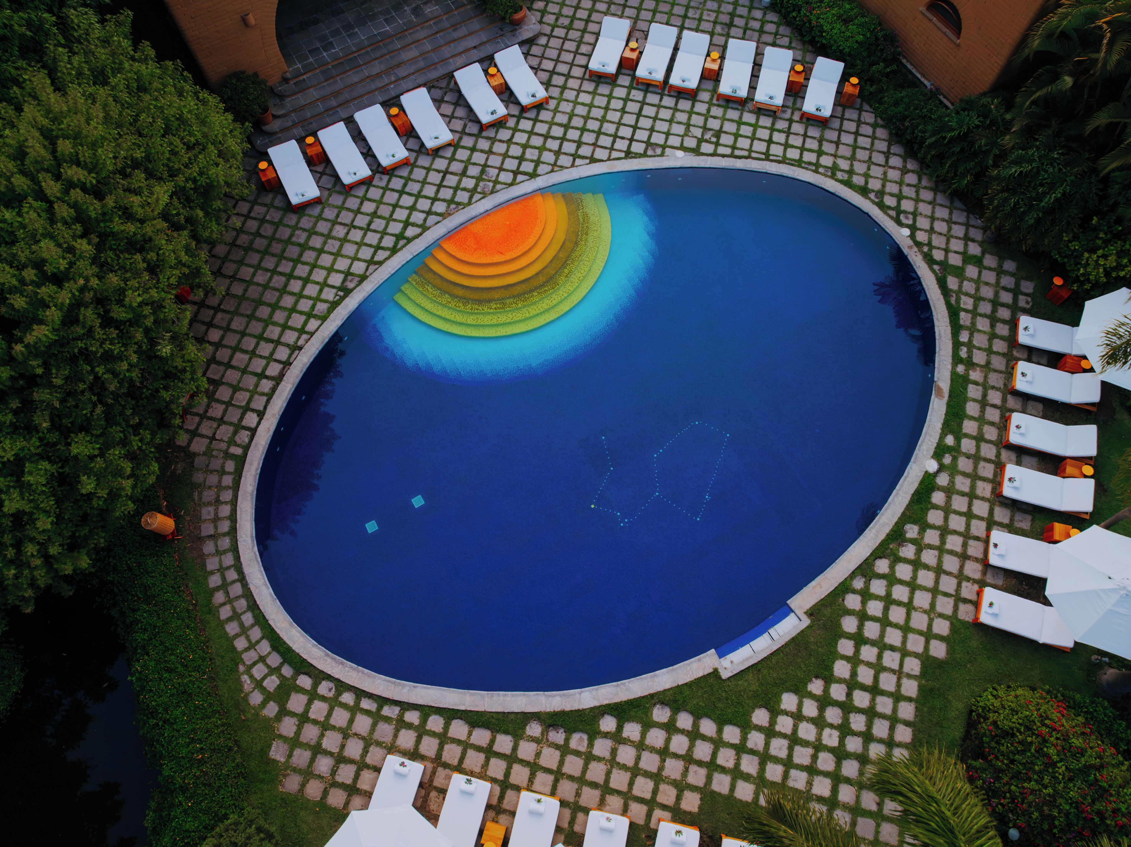 An aerial view of a pool with a circular design, surrounded by lounge chairs and potted plants.