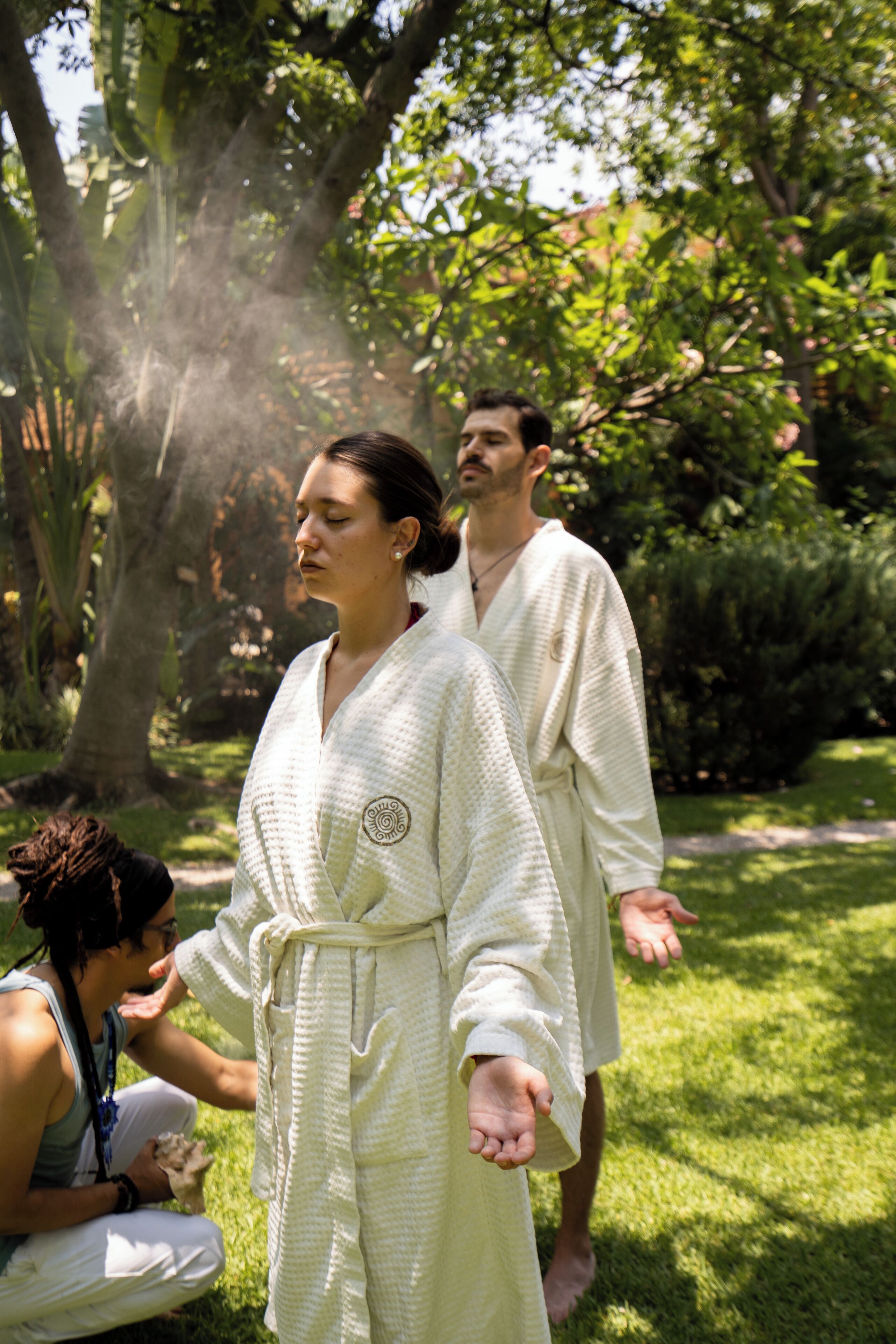 A person in a white robe standing in a lush garden with trees and grass.