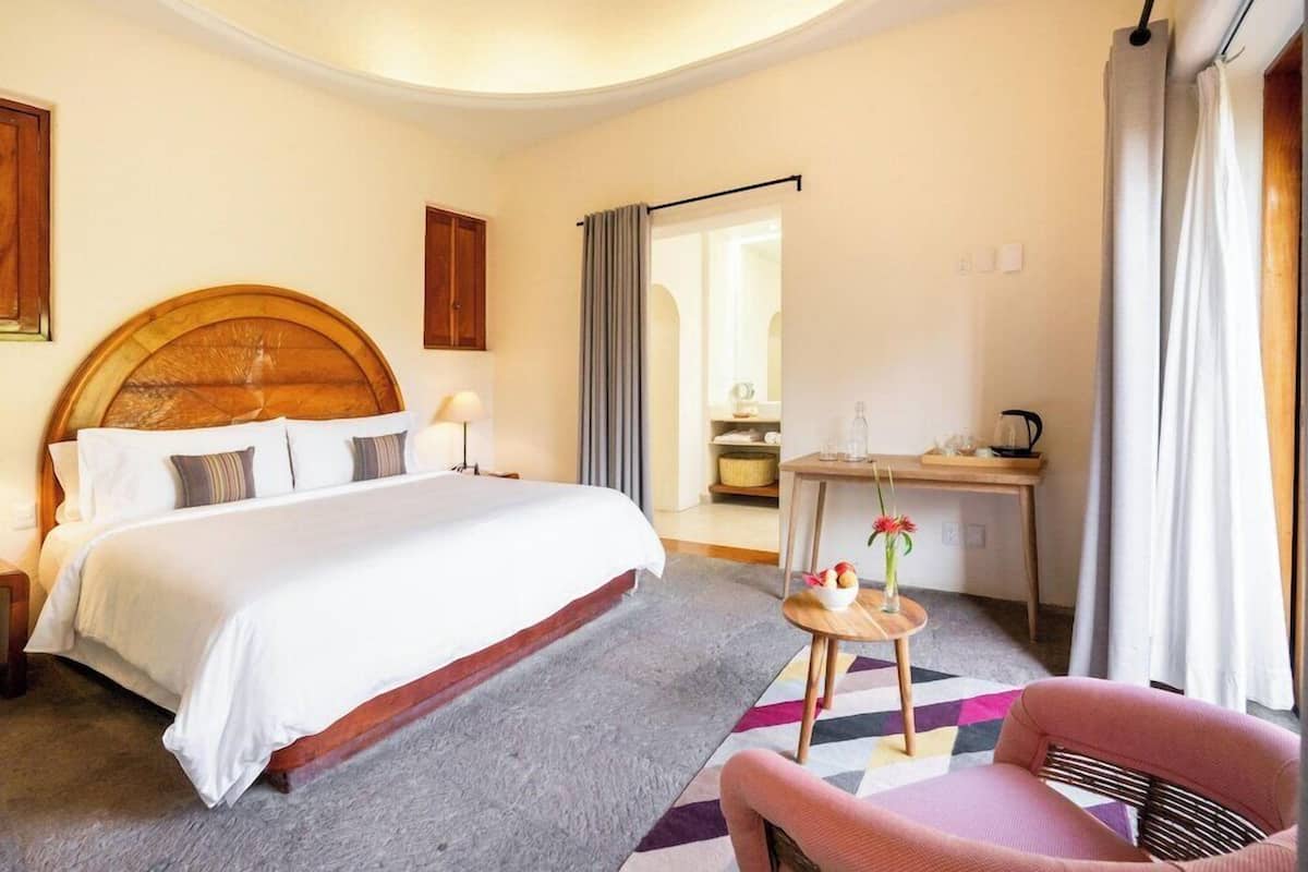 A hotel room with a large bed, a desk, a chair, and a small table with a vase of flowers.